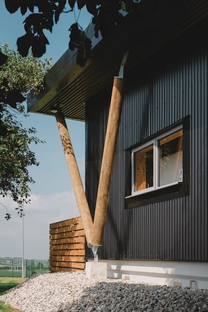 corner view of black metal clad building showing wooden support posts