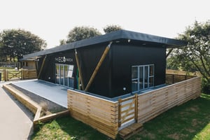 corner view of black metal clad building with wooden fence in foreground