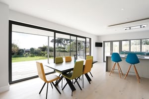 dining table with yellow and green chairs around and large sliding door to garden behind