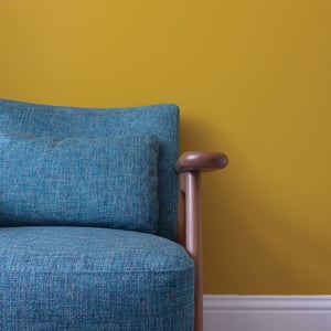 grey blue armchair in front of mustard yellow wall