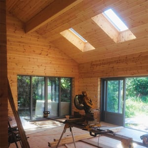 timber frame home in construction with workbench and saw in foreground and light pouring in from two roof lights